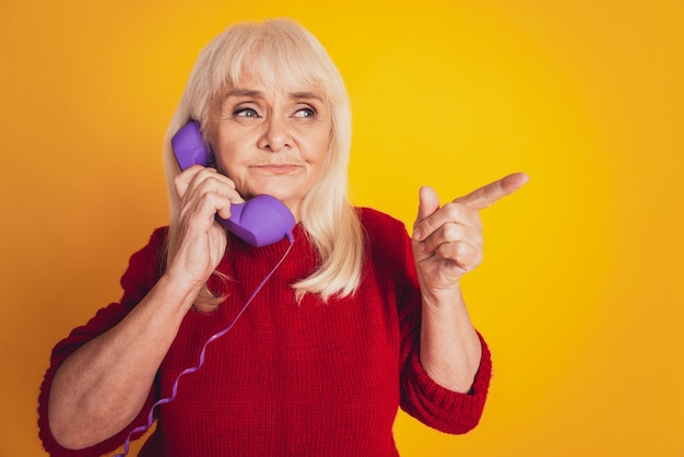 Mujer madura, hablando por teléfono, señalar con el dedo índice el espacio vacío sobre fondo amarillo