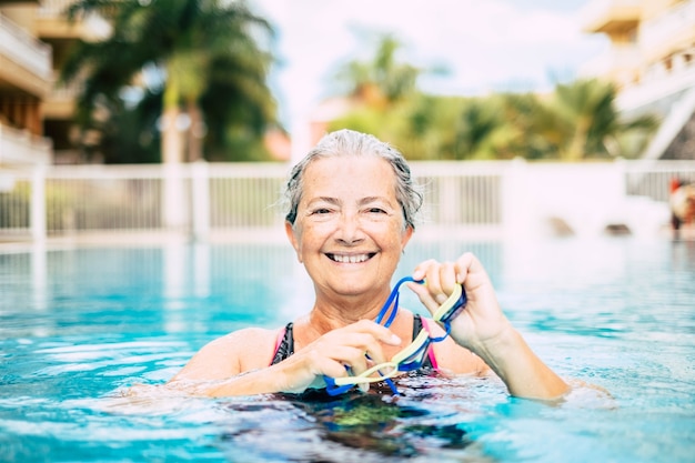Una mujer madura haciendo actividad en la piscina nadando y entrenando sola - mirando a la cámara y sonriendo