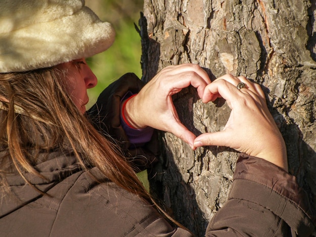 Foto mujer madura haciendo forma de corazón en el tronco del árbol