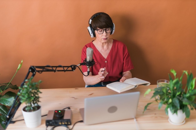 Mujer madura haciendo una grabación de podcast para su programa en línea Atractiva mujer de negocios usando auriculares frente al micrófono para una transmisión de radio