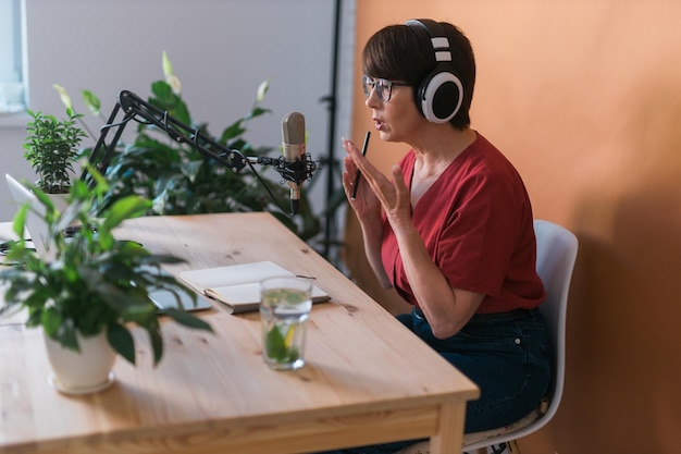 Mujer madura haciendo grabación de podcast para su programa en línea atractiva mujer de negocios usando auriculares