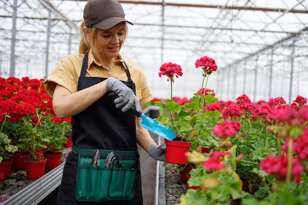 Mujer madura en un invernadero cuidando macetas con flores