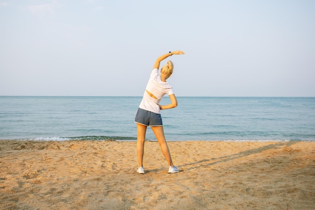 Mujer madura mayor activa que se extiende en la playa estilo de vida saludable y fitness