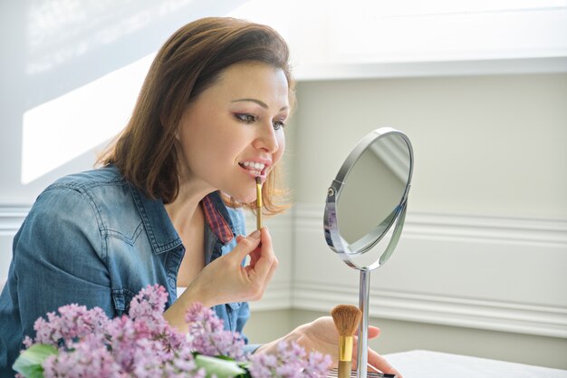 Mujer madura mirando su rostro en el espejo, haciendo maquillaje