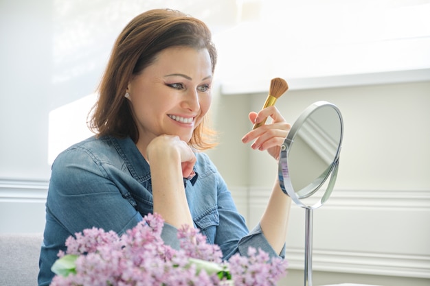 Mujer madura mirando su rostro en el espejo, haciendo maquillaje