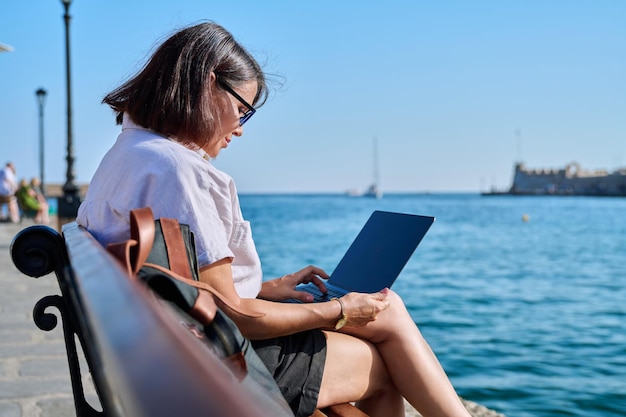 Mujer madura de negocios sentada al aire libre usando una laptop