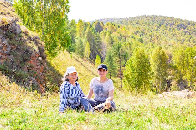 Mujer madura y niña sentada en la ladera de una montaña en un día cálido y soleado