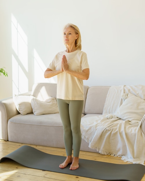 Mujer madura pacífica meditando mientras practica yoga en la estera en casa