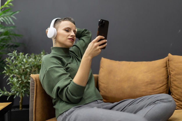 Mujer madura con el pelo corto tumbado en el sofá escuchando música con auriculares mirando