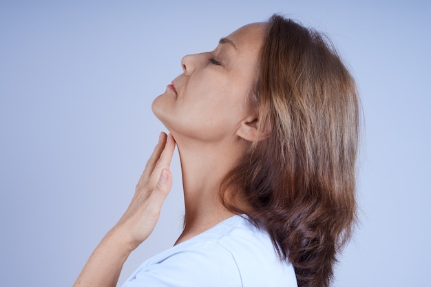 Una mujer madura de perfil, tocándose el suave cuello con la mano. Cuidado de la piel del rostro en la edad adulta