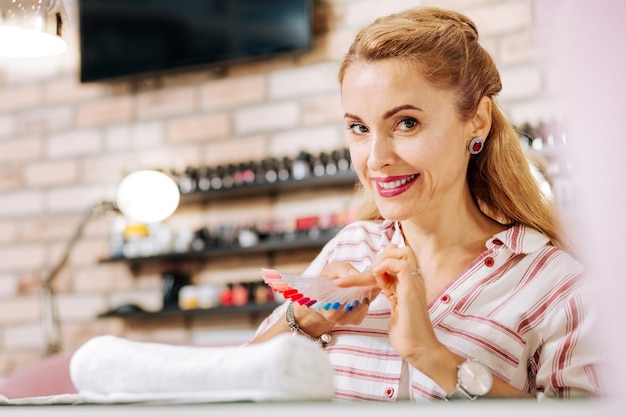 Mujer madura positiva mirando a la cámara y optando por el color del esmalte de uñas