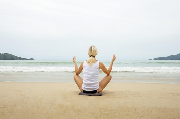 Mujer madura practicando yoga en la playa