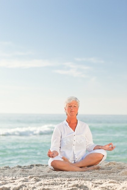 Foto mujer madura practicando yoga en la playa