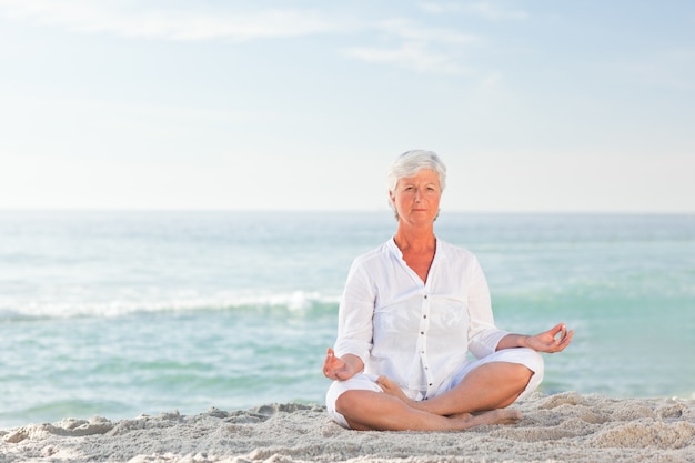 Foto mujer madura practicando yoga en la playa