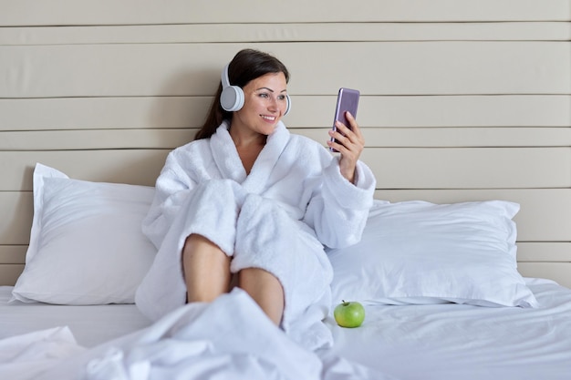 Mujer madura que habla feliz en auriculares usando un teléfono inteligente para videollamadas