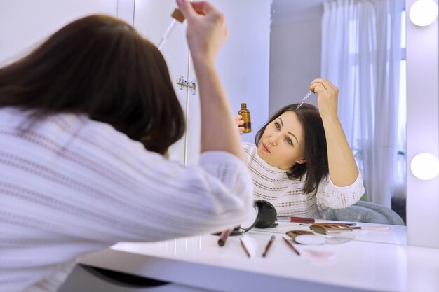 Mujer madura que trata el cuidado del cabello con productos cosméticos y médicos