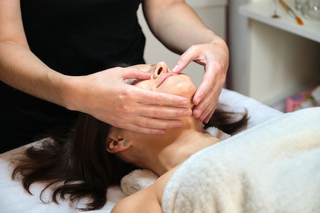 Mujer madura recibe masaje de cara y cuello en el salón de belleza spa. Cosmetología, tratamiento, asistencia sanitaria, cuidado de la piel facial y corporal, mujeres de mediana edad