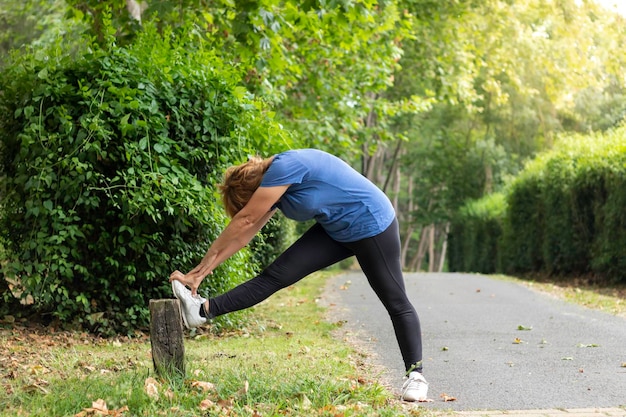 Mujer madura en ropa activa haciendo ejercicio para estirar las piernas mientras disfruta del entrenamiento en un entorno natural