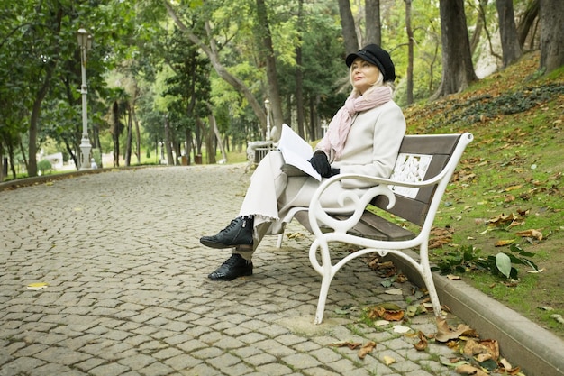 Una mujer madura sentada en un banco del parque piensa y lee un libro en un hermoso día de otoño