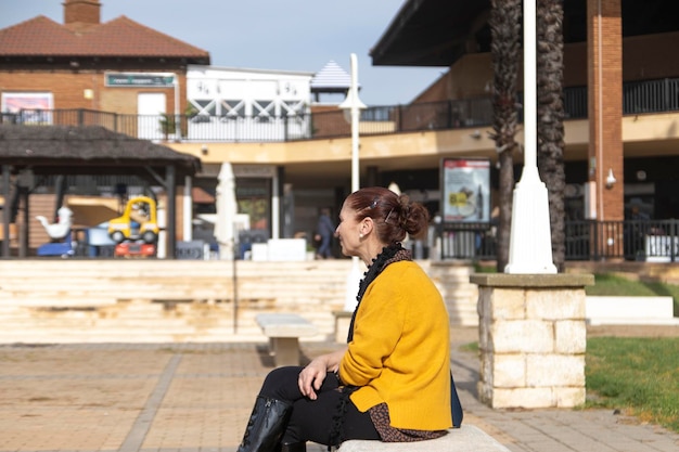 Mujer madura sentada en un banco en una plaza. Concepto de soledad.