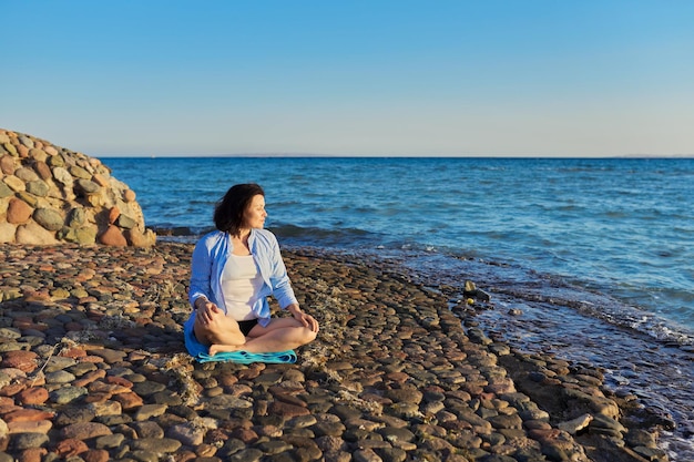 Mujer madura sentada en posición de loto meditando en la playa