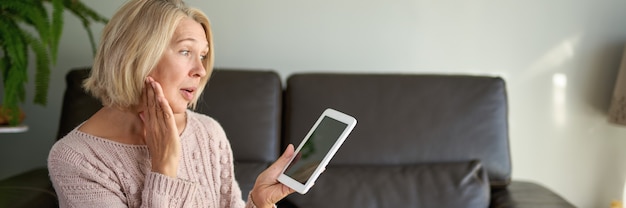 Mujer madura sentada en el sofá y con tableta digital.