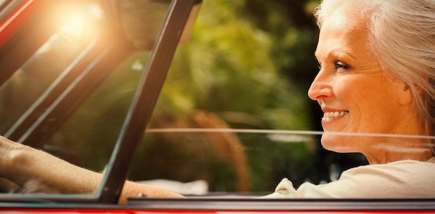 Foto mujer madura sonriente conduciendo convertible rojo durante el día soleado