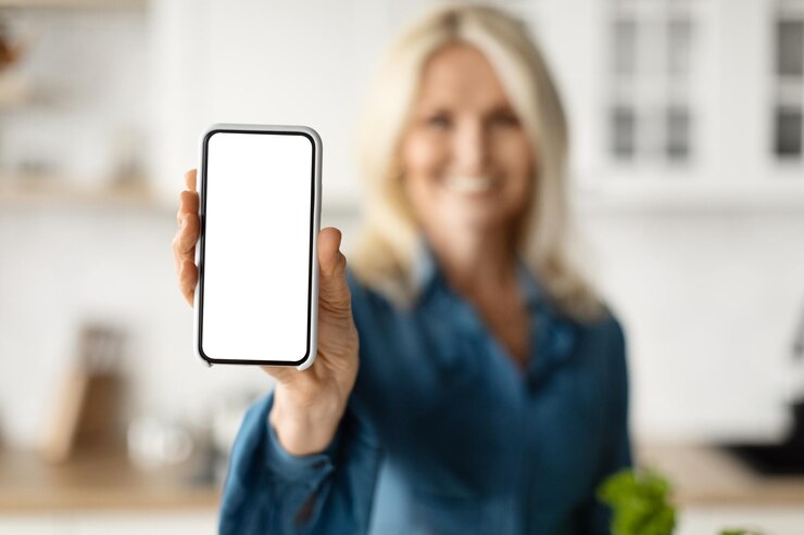 Mujer madura sonriente que muestra la aplicación móvil de publicidad de teléfonos inteligentes en blanco para la entrega de comestibles
