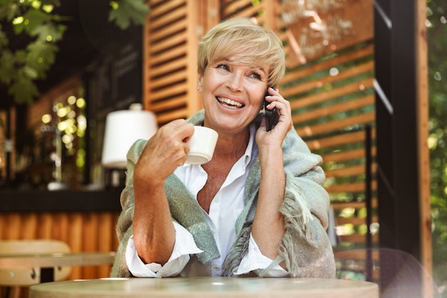 Mujer madura sonriente que sostiene el teléfono móvil