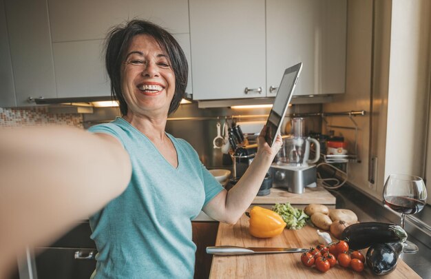 Foto mujer madura sonriente usando una tableta digital en la cocina