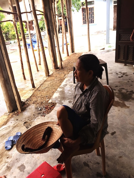 Mujer madura de toda la longitud con sombrero cónico de estilo asiático sentada en una silla