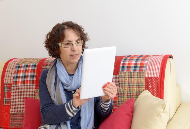 Foto mujer madura usando una tableta digital mientras está sentada en el sofá en casa