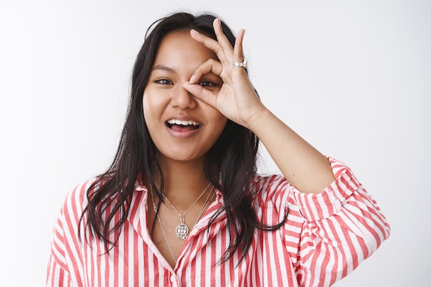 Mujer malaya optimista que muestra un buen gesto sobre los ojos y una sonrisa sorprendida y emocionada
