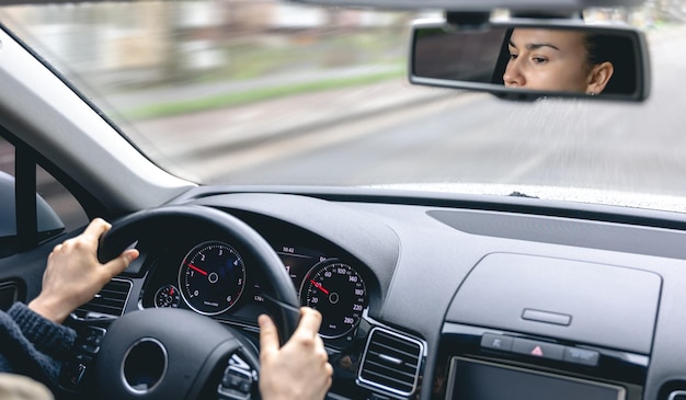 La mujer maneja un auto reflejado en el espejo retrovisor