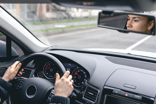 La mujer maneja un auto reflejado en el espejo retrovisor