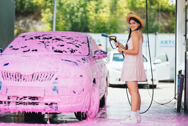 Mujer con manguera en coche cubierta de espuma rosa