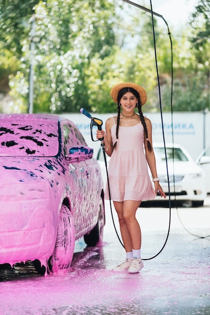 Mujer con manguera en coche cubierta de espuma rosa