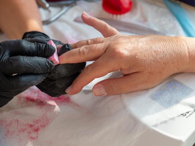 Mujer de manicura usando esponja de pulido quitando el esmalte viejo para pintura de uñas permanente