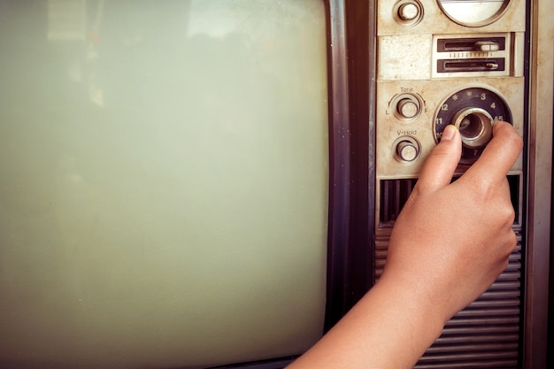 Mujer de mano de ajuste fino de la televisión de época con el botón de control. Imagen retra procesada.