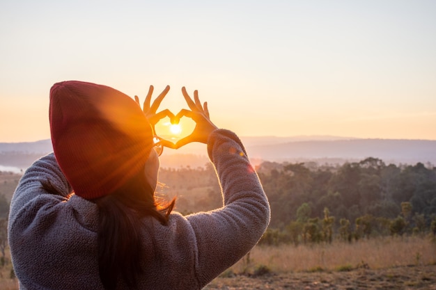 Foto una mujer con una mano en forma de corazón con el sol en medio de la forma de corazón.