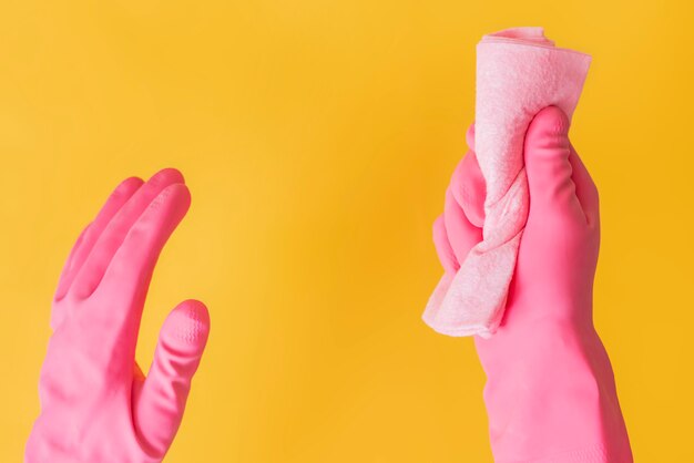 Mujer mano en guantes de color rosa con un trapo contra el fondo de color sólido.