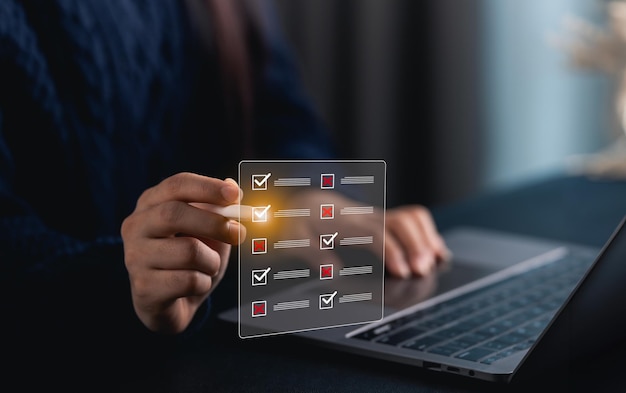 Mujer de mano en primer plano usando una lista de comprobación digital en una computadora portátil mientras administra tareas y proyectos para una organización eficaz en un espacio de trabajo moderno con luz ambiental
