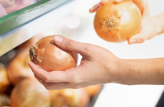 Foto mujer con la mano sosteniendo cebolla eligiendo para preparar el alimento material en el estante de la canasta en el supermercado