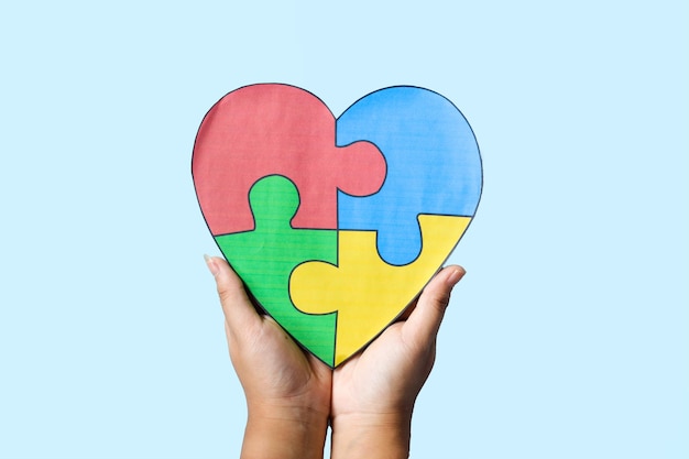 Mujer con la mano sosteniendo el corazón hecho de rompecabezas de color en fondo azul Concepto de trastorno autista