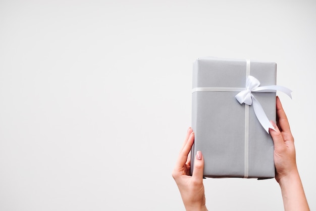 Mujer mano sujetando caja de regalo con regalo de cumpleaños sobre fondo blanco.