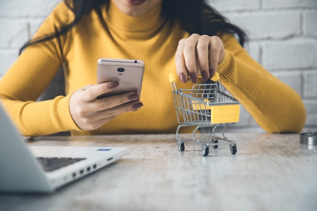 Foto mujer mano teléfono y canasta en computadora en mesa