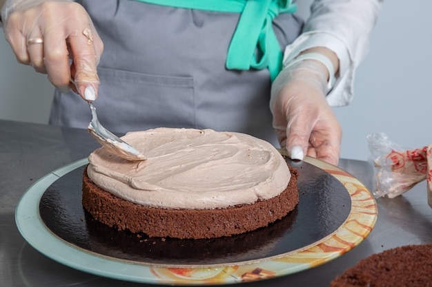 mujer manos chef untando crema en la primera capa de pastel de chocolate. haciendo pastel de capas de chocolate.