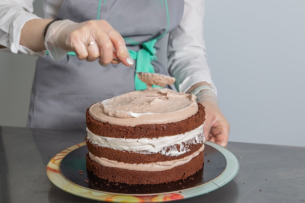 mujer manos chef untando crema en la tercera capa de pastel de chocolate.