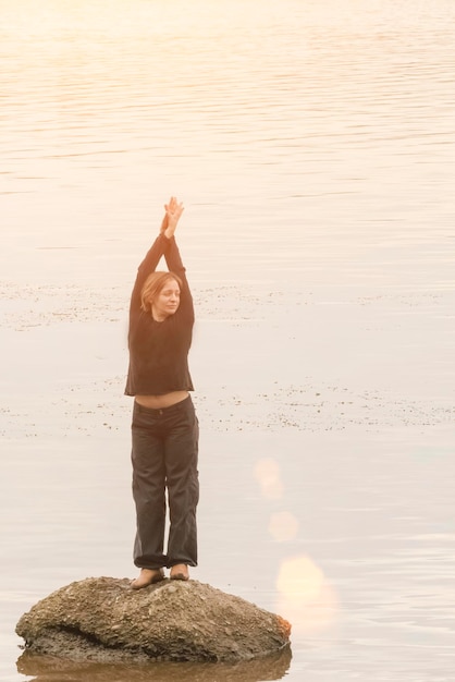 Mujer con las manos levantadas sobre una roca en medio del río soleado