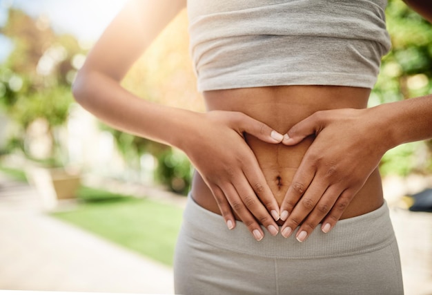 Mujer de manos en el parque y el estómago, dieta y naturaleza para la salud intestinal, lipo y bienestar para el entrenamiento corporal, salud en el gimnasio y abdominoplastia, niña con el signo de la mano del corazón en el abdomen para objetivos de ejercicio